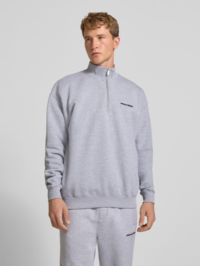 Męski model nosi Relaxed Fit Sweatshirt aus Baumwoll-Mix od PEGADOR, jasnoszary kolor, wyhaftowane logo, ozdobne szwy, kołnierz zapinany, długi rękaw, prążkowane wykończenia, widoczna struktura materiału, Ganzkörperansicht von vorne.