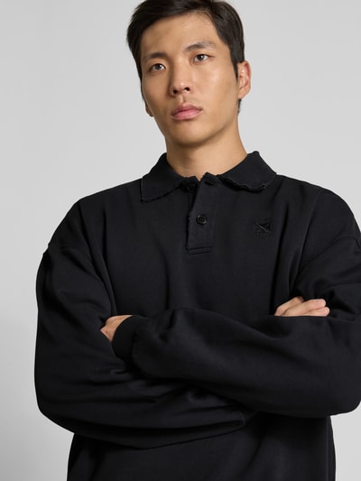 Männermodel trägt Regular Fit Poloshirt aus Baumwoll-Mix von VETEMENTS in Schwarz, Sweat, Polokragen, Nahaufnahme Oberkörper.