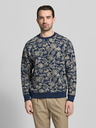 Männermodel trägt Sweatshirt im Allover-Look mit Rundhalsausschnitt von Scotch & Soda, puur katoen, regular fit, all-over look, ruglengte maat M 67 cm, mouwlengte maat M 68 cm, donkerblauw met beige bloemenpatroon, ganzkörperansicht von vorne.