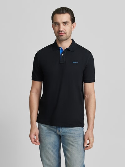Męski model nosi Regular Fit Poloshirt mit Logo-Stitching od Gant, czarny kolor, bawełniany elastyczny materiał, krótki rękaw, przód, krój regular fit, długość pleców 70 cm w rozmiarze M, całopostaciowy widok z przodu.