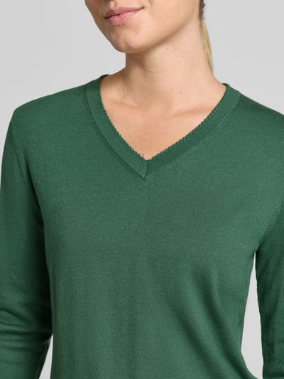 Frauenmodel trägt Pullover aus Viskose-Mix mit V-Ausschnitt von Christian Berg Woman in dunklem Grün, Nahaufnahme Oberkörper, gerader Schnitt, gerippte Abschlüsse, Rückenlänge 46 cm, Ärmellänge 63 cm.