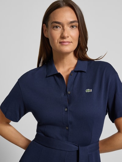 Frauenmodel trägt Tailliertes Freizeitkleid aus reiner Baumwolle von Lacoste, unifarben dunkelblau, Piqué-Textur, Nahaufnahme Oberkörper.
