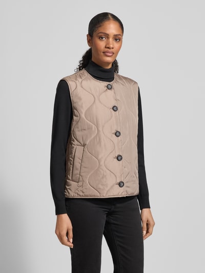 Frauenmodel trägt Regular Fit Steppweste mit einreihiger Knopfleiste Modell 'MILLIE' von Vero Moda, unifarbene Optik, seitliche Eingrifftaschen, gesteppte Textur, Ganzkörperansicht von vorne.
