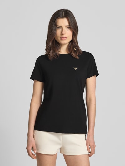 Modelka nosi Regular Fit T-Shirt mit Logo-Applikation Modell 'Colette' od Guess Activewear, bawełna elastyczna, krój regular fit, aplikacja logo, czarny kolor, okrągły dekolt, długość tyłu w rozmiarze S: 60 cm, zdjęcie całej sylwetki z przodu.