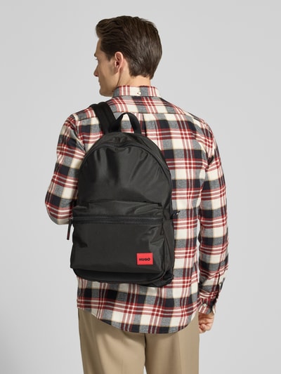 Männermodel trägt Rucksack mit Label Patch Modell 'ETHON 3,0' von HUGO, schwarz, Reißverschluss, Vordertasche, Ganzkörperansicht Rückansicht.