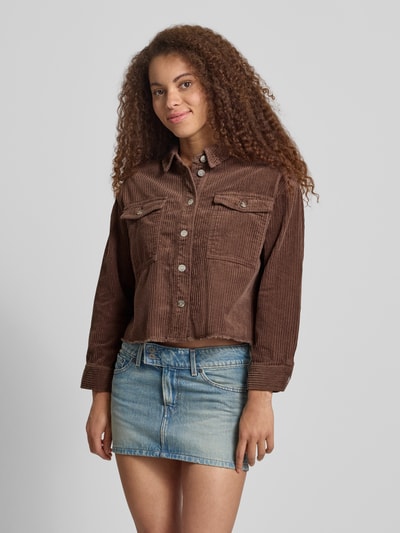 Frauenmodel trägt Boxy Fit Cordjacke aus reiner Baumwolle Modell 'MARINA-ENY LIFE' von Only in Braun mit Brusttaschen und Fransen, Ganzkörperansicht von vorne.