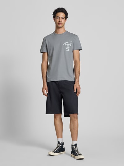 Männermodel trägt Regular Fit T-Shirt aus reiner Baumwolle von Tommy Jeans in Grau mit Label-Schriftzug, unifarben, Ganzkörperansicht von vorne.
