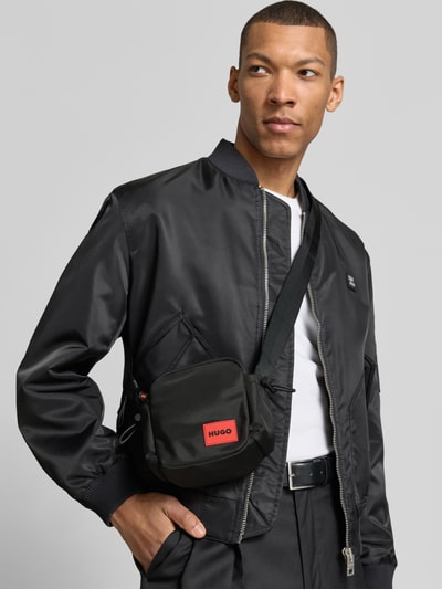 Männermodel trägt Umhängetasche mit Label-Patch Modell 'ETHON 3.0 NEW NSzip' von HUGO, Optik: Unifarben, Reißverschluss, Hauptfach, Einschubfach innen, Seitenfächer, Label-Patch, Schulterriemen, Ganzkörperansicht von vorne.