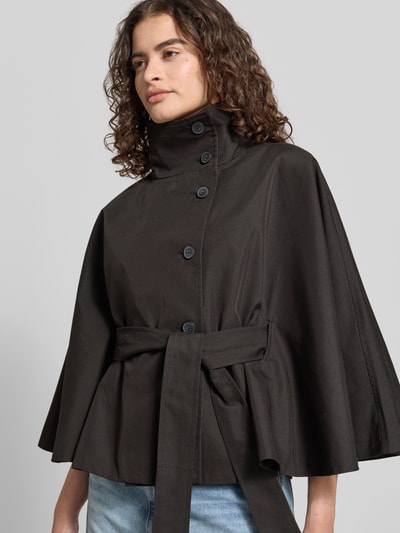 Vrouwenmodel draagt Trenchjacke met Stehkragen Modell 'Isa' van Gina Tricot in zwart katoenmix, getailleerd model, knoopsluiting, kimonomouwen, strikceintuur, nahaufnahme bovenlichaam.
