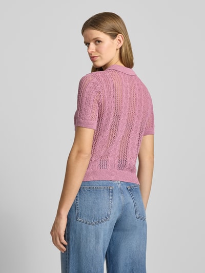 Frauenmodel trägt Slim Fit Poloshirt in Strick-Optik Modell 'Ajour' von Review in Rosa, Lochmuster, Jeans, Ganzkörperansicht Rückansicht.