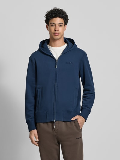 Męski model nosi Sweatjacke mit Kapuze Modell 'TAURASI' od Ellesse, bawełniana mieszanka, luźny krój, kolor granatowy, zamek, logo, kieszenie, ściągacze, widok całej sylwetki z przodu.