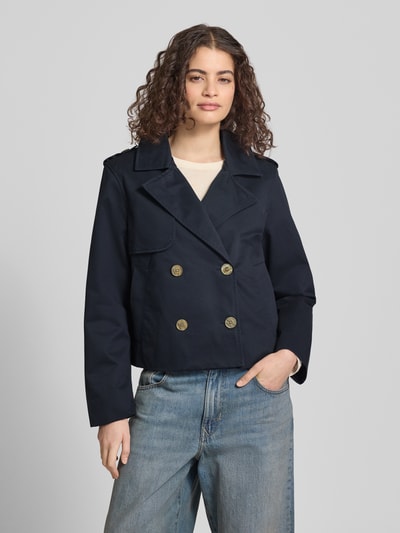 Vrouwenmodel draagt 'Regular Fit Trenchcoat mit Umlegekragen' van Review in donkerblauw, zuiver katoen, regular fit, reverskraag, dubbele knoopsluiting, steekzakken, ruglengte 55 cm, schouderbreedte 45 cm, borstwijdte 53 cm, mouwlengte 62 cm, vooraanzicht bovenlichaam.
