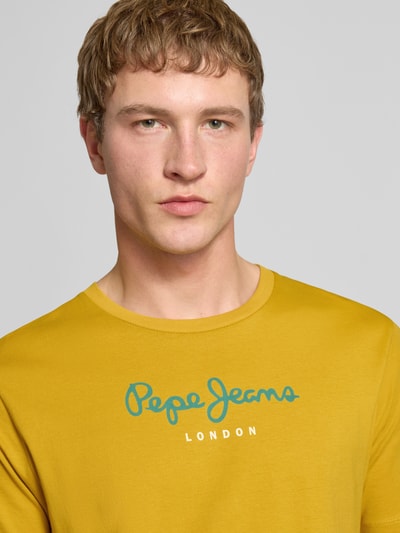 Męski model nosi Regular Fit T-Shirt aus reiner Baumwolle Modell 'EGGO' od Pepe Jeans, jednolity żółty jersey, nadruk z logo, zbliżenie na górną część ciała.