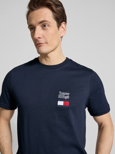Männermodel trägt Regular Fit T-Shirt aus reiner Baumwolle Modell 'BRAND LOVE TEXT' von Tommy Hilfiger in Dunkelblau mit Logo-Stitching, Nahaufnahme Oberkörper.