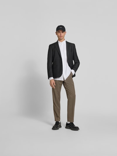 Männermodel trägt Straight Fit Stoffhose mit Woll-Anteil von Filippa K in Beige, kombiniert mit schwarzem Blazer, Ganzkörperansicht von vorne. Elastischer Material-Mix, Bundfalten, elastischer Bund, Eingrifftaschen.