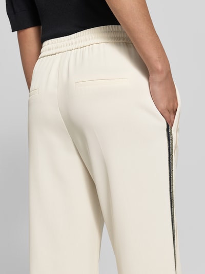 Vrouwenmodel draagt Hose mit elastischem Bund und Galonstreifen van Marc Cain in regular fit met elastische band, persplooien en galonstrepen, kleur licht crème, detailaufnahme achterkant