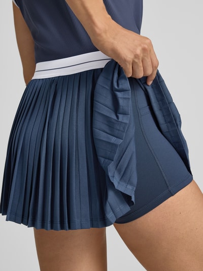 Frauenmodel trägt Minirock mit integrierten Shorts Modell 'Clemency' von VARLEY, Dunkelblau, A-Linie, Falten, Nahaufnahme Oberschenkel.