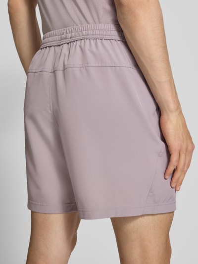 Mannenmodel draagt Shorts met Logo-Print en Steekzakken van NIKE TRAINING in lichtpaars, recht model, elastische band met trekkoord, zij-steekzakken, bandwijdte maat M 41 cm, binnenbeenlengte maat M 19 cm, detailopname van achteren.