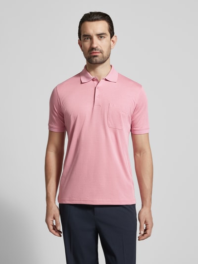 Męski model nosi Relaxed Fit Poloshirt aus Baumwoll-Mix von RAGMAN w kolorze jasnoróżowym z kołnierzykiem polo, brustasza z wyhaftowanym logo, krótki rękaw, elastyczne zakończenia rękawów, długość tyłu w rozmiarze M: 70 cm, mieszanka bawełny; całkowity widok z przodu