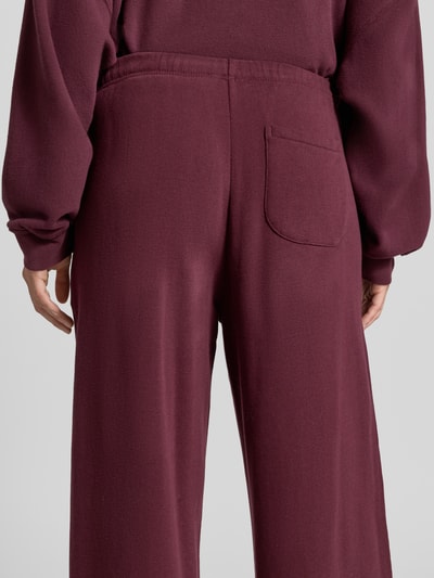 Frauenmodel trägt Straight Fit Sweatpants aus elastischem Baumwoll-Mix von American Vintage, dunkelrot, Modell 'ATUBAY', Detailaufnahme Rückansicht. Damen Sweatpants mit Bund und Tunnelzug, glatte Struktur.