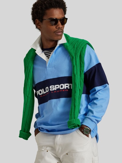 Männermodel trägt Regular Fit Poloshirt aus reiner Baumwolle von Polo Ralph Lauren in Hellblau mit Logo-Schriftzug, Rippenstruktur, Ganzkörperansicht von vorne.