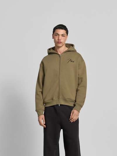 Männermodel trägt Oversized Sweatjacke aus Baumwolle von RHUDE in Olivgrün mit Zweiwege-Reißverschluss und Label-Stitching, elastische Abschlüsse, Rückenlänge 70 cm, Schulterbreite 62 cm, Ärmellänge 66 cm, Ganzkörperansicht von vorne.