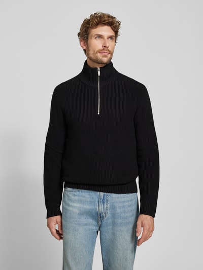 Männermodel trägt Slim Fit Strickpullover aus reiner Baumwolle mit Troyer-Kragen von MCNEAL, schwarze Farbe, gerippte Textur, Ganzkörperansicht von vorne.