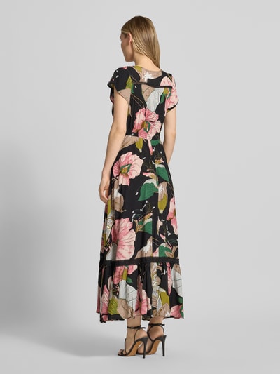 Frauenmodel trägt Maxikleid aus Viskose mit V-Ausschnitt von Apricot, floraler Print in Schwarz mit Volants, Tailliert, Eingrifftaschen, Rückenlänge 130 cm, Brustweite 43 cm, Ärmellänge 11 cm, Ganzkörperansicht Rückansicht.
