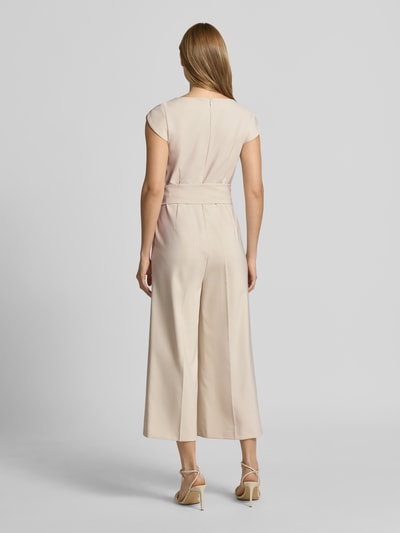 Modelka kobieca nosi Regular Fit Jumpsuit mit Bügelfalten von Betty Barclay, elastyczna mieszanka materiałów, kolor jasny beż, kanty, odpinana materiałowa tasiemka, z krótkim rękawem, długość tyłu w rozmiarze 36: 133 cm, szerokość w rozmiarze 36: 47 cm, całkowita długość w rozmiarze 36: 40 cm, długość wewnętrzna nogawki w rozmiarze 36: 62 cm, widok całej sylwetki z tyłu