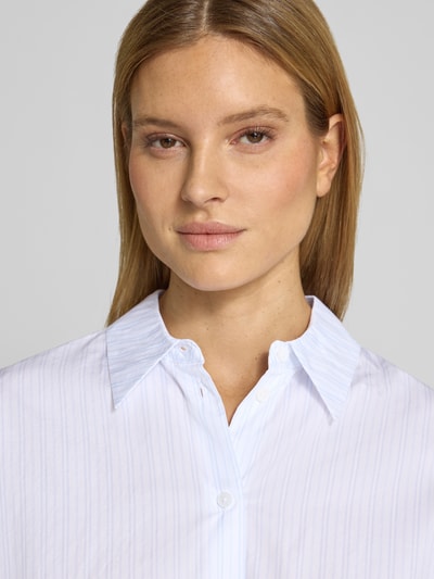 Kobiece modelka nosi bluzkę z bawełny o kroju relaxed fit Relaxed Fit Bluse mit verlängertem Rückenteil Modell 'CLOELIA' od Drykorn, kołnierzyk koszulowy, białe i jasnoniebieskie paski, długość tyłu 66 cm, długość rękawów 52 cm, zbliżenie na górną część ciała
