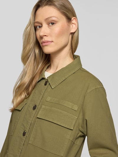 Vrouwenmodel draagt Jacke mit Pattentaschen und Label-Detail van camel active, olijfgroen, kentkraag, knoopsluiting, borstzakken, stretch katoenmix, rechte fit, detailopname bovenlichaam.