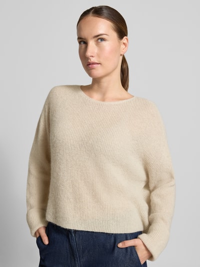 Frauenmodel trägt Strickpullover aus Alpaka-Mix Modell 'MENY' von DRYKORN, beige, grobe Rippenstruktur, lockere Passform, Nahaufnahme Oberkörper.