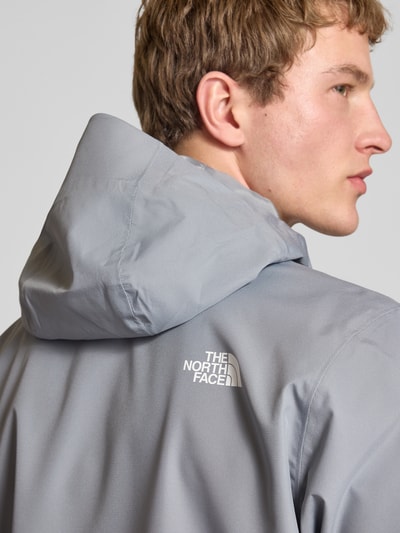 Männermodel trägt Jacke mit Kapuze von The North Face in Hellgrau mit Label-Print und verdecktem Reißverschluss, Nahaufnahme Rückansicht.