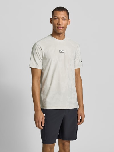 Mannelijk model draagt T-Shirt met Rundhalsausschnitt und Label-Detail van EA7 Emporio Armani, materiaal-mix met stretch, regular fit, labeldetail op borst, ruglengte bij maat M 69 cm, lichte kleur met subtiele structuur, volledige lichaamsaanzicht van voren