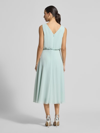 Modelka nosi Knielanges Cocktailkleid mit Wasserfall-Ausschnitt von Christian Berg Cocktail, szyfon, taliowany krój, długość do kolan, szerokie ramiączka, kopertowy styl dołu, zapięcie na haftkę i zamek błyskawiczny z tyłu, długość tyłu w rozmiarze 36: 120 cm, szerokość w rozmiarze 36: 45 cm, pastelowozielony, gładka tekstura. Ganzkörperansicht Rückansicht.
