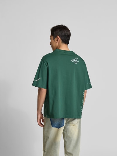 Männermodel trägt Oversized T-Shirt aus Bio-Baumwolle von MAISON KITSUNÉ in Grün mit Label-Print, Rückenansicht, Ganzkörperansicht Rückansicht.