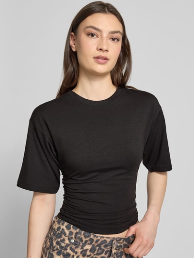 Frauenmodel trägt T-Shirt in tailliertem Schnitt Modell 'ELORA' von JJXX aus Baumwoll-Mix mit Modal-Anteil, Rundhalsausschnitt, schwarze Farbe, Ganzkörperansicht von vorne.