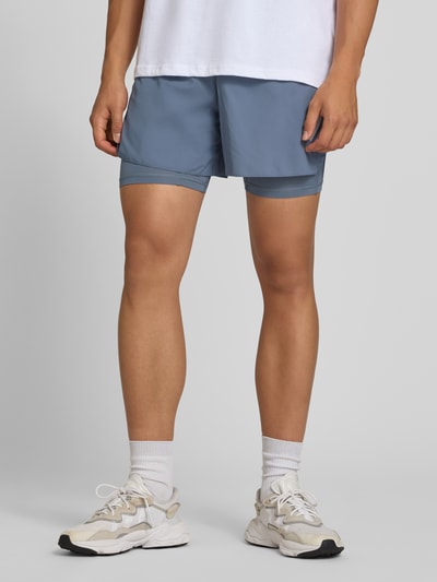 Männermodel trägt blaue Regular Fit Sportshorts mit Logo-Print Modell 'ADI365/// 2i1 M' von adidas, adidas Training, Nahaufnahme Oberschenkel.