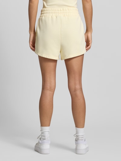 Frauenmodel trägt High Waist Sweatshorts mit Logo-Stitching Modell 'WILUNA' von Pegador in hellem Gelb, Baumwoll-Mix, elastischer Bund, Ganzkörperansicht Rückansicht.