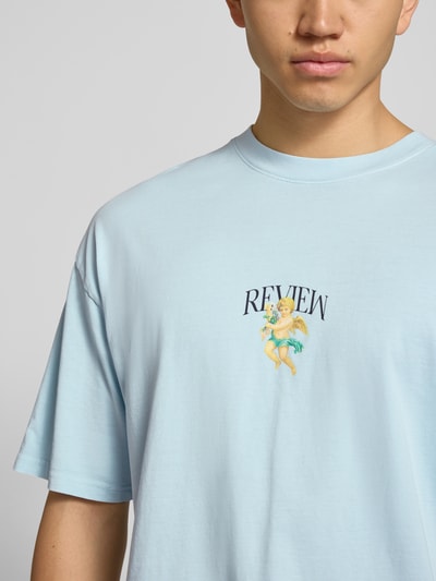 Männermodel trägt T-Shirt mit überschnittenen Schultern von REVIEW in Hellblau, Reine Baumwolle, Label-Print, Lockerer-Schnitt, Nahaufnahme Oberkörper.