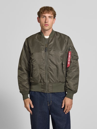 Männermodel trägt Bomberjacke mit Pattentaschen und Label-Applikation von Alpha Industries, olivegrün, glatte Oberfläche, Ganzkörperansicht von vorne. Regular Fit, Stehkragen, Reißverschluss, Maße für Größe M: Rückenlänge 69 cm, Schulterbreite 44 cm, Brustweite 54 cm, Ärmellänge 64 cm.