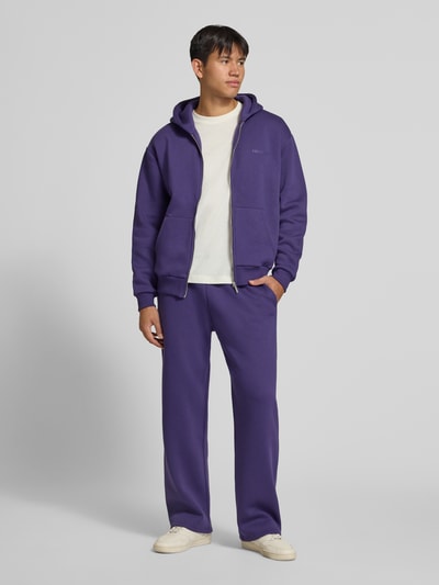 Männermodel trägt Relaxed Fit Sweatjacke aus Baumwoll-Mix mit Label-Detail von REVIEW in Lila mit Kapuze, elastischen Abschlüssen, Känguru-Tasche, Ganzkörperansicht von vorne.