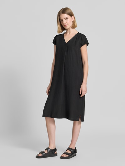 Frauenmodel trägt knielanges Leinenkleid mit V-Ausschnitt Modell 'Ina' von Soyaconcept aus Leinen-Mix mit Viskose-Anteil, Loose-Fit, Schwarz, seitliche Schlitze, glatte Textur, Knielänge, Ganzkörperansicht von vorne.