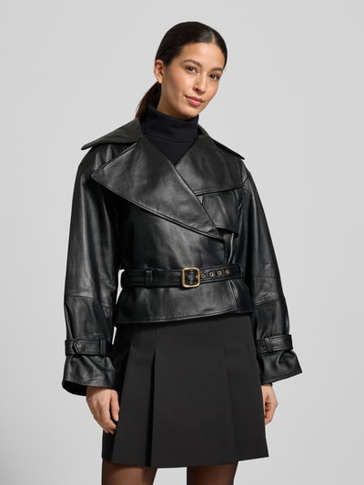 Modelka kobieta ma na sobie Slim Fit Lederjacke aus echtem Lammleder Modell 'LANITTE' od HUGO, krój slim fit, czarny gładki skórzany materiał, pasek w talii z klamrą, napy przy mankietach, naszywka z logo, widok całej sylwetki z przodu.