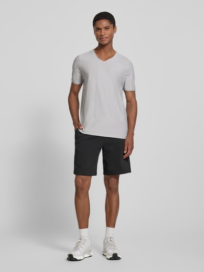 Męski model nosi T-Shirt mit V-Ausschnitt und Rollsaum od MCNEAL z bawełny, krój regular fit, dekolt w serek, długość tyłu 81 cm, jasnoszary, gładka tekstura, prosty krój, całopostaciowy widok z przodu.