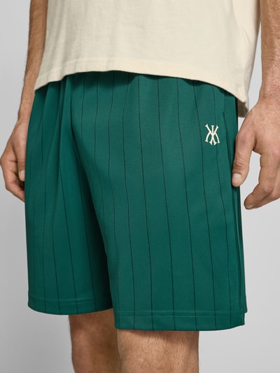 Männermodel trägt Herren Shorts mit elastischem Bund Modell 'Insignia Shadow' von KARL KANI im Allover-Look, grün, Nahaufnahme Oberschenkel. Bundweite bei Größe M: 38 cm, Innenbeinlänge: 19 cm, Regular-Fit.
