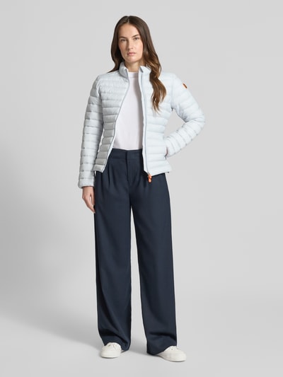 Modelka kobieca nosi jasnoniebieską Slim Fit Steppjacke z wypełnionym stójką model 'Carly' od SAVE THE DUCK, prosty deseń, gładka faktura, dwukierunkowy zamek błyskawiczny, kieszenie boczne na zamek, długość tyłu w rozmiarze S: 58 cm, szerokość ramion w rozmiarze S: 39 cm, szerokość w rozmiarze S: 45 cm, długość rękawa w rozmiarze S: 61 cm, krój slim fit, widok całopostaciowy z przodu.