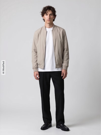 Männermodel trägt hellbeige Regular Fit Bomberjacke mit Baseball-Kragen Modell 'CHARLES' von Selected, Herren Bomberjacke, Ganzkörperansicht von vorne, KI-modifiziertes Bild.