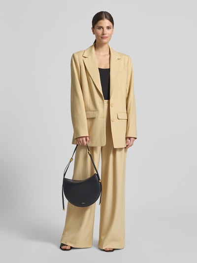Frauenmodel trägt Shoulder Bag mit Logo-Print Modell 'Moonstone' von FURLA in Dunkelblau, beige Anzug, Hauptfach mit Magnetverschluss, verstellbarer Schulterriemen, Ganzkörperansicht von vorne. Breite 31 cm, Länge 20 cm, Tiefe 3 cm, Länge Schulterriemen 57 cm.