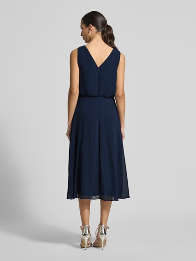 Frauenmodel trägt knielanges Cocktailkleid mit Wasserfall-Ausschnitt von Christian Berg Cocktail aus dunkelblauem Chiffon, Taillierter Schnitt, Knielänge, Breite Träger, Saum in Wickeloptik, rückseitiger Haken- und Reißverschluss, Rückenlänge bei Größe 36: 120 cm, Brustweite bei Größe 36: 45 cm, Ganzkörperansicht Rückansicht.